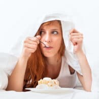 Fotografía de mujer joven comiendo escondida bajo sabanas